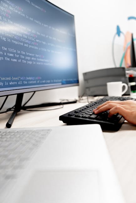 Close-up image of a computer screen displaying lines of HTML code with colorful syntax highlighting, including tags, attributes, and comments. The background shows a dark theme with text in shades of 